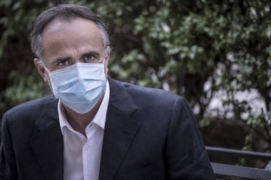 Koruyucu maskeli bir beyefendi bir bankta oturmuş depresif görünüyor.