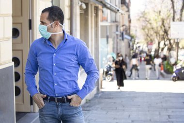 Mavi gömlekli adam, yüz maskesi şehir bağlamında sıkıdır.