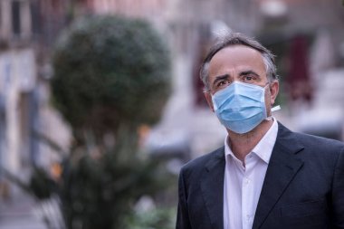 Şehir bağlamında koruyucu maskeli takım elbiseli bir adam.