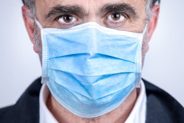 Arka planda izole edilmiş, cerrahi maske, ceket ve gömlek giyen bir adamın portresi.