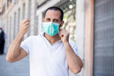 Siyah saçlı, beyaz polo giyen adam kaldırımda maske takıyor.