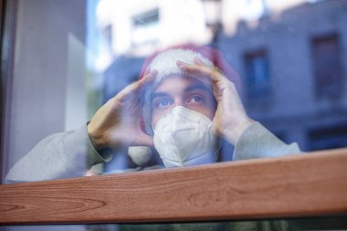 Yüz maskeli adam ve pencereye bakan Noel şapkalı adam.