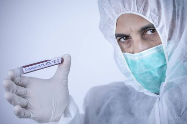 Koruyucu giysili ve maskeli doktor koronavirüs kan testi için tüp tutuyor.