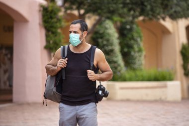 Siyah saçlı, kolsuz tişörtlü, sırt çantalı ve koruyucu maskeli bir adam.