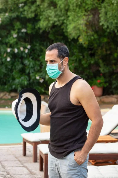 在一家宾馆的游泳池里 身穿夏装 头戴帽子 戴着外科口罩的黑头发男子放松了下来 — 图库照片