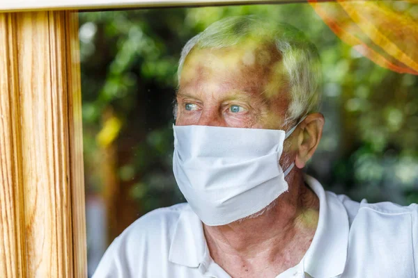 Starší Muž Lékařské Masce Při Pohledu Okna Doma — Stock fotografie