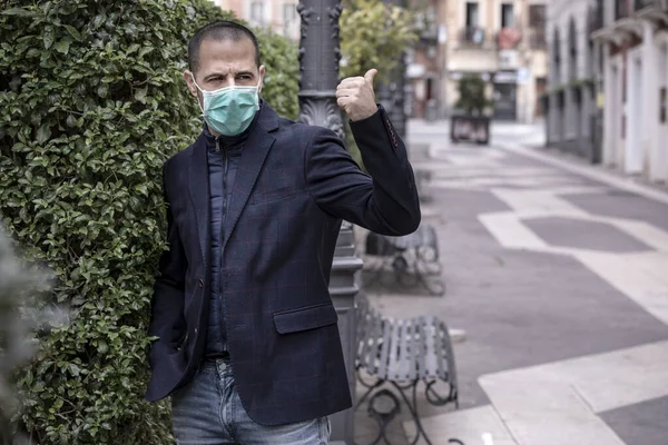 身穿夹克 戴着绿色防毒面具的男孩要求在城市里带着大拇指搭便车 — 图库照片