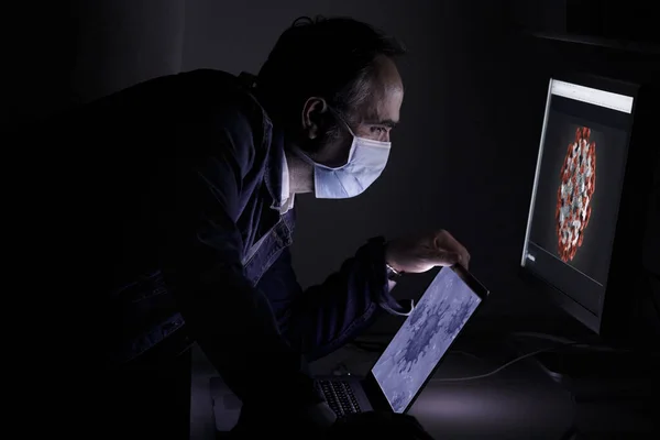man with a mask and a computer in his workplace at night