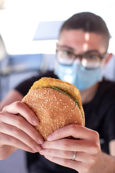 戴防护面具的年轻人吃汉堡包 — 图库照片