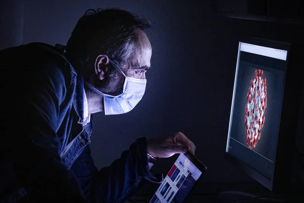 man with a mask and a computer in his workplace at night