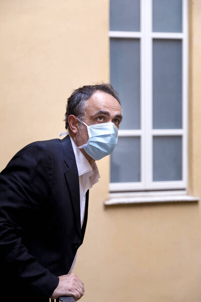 manager with protective face mask, looks out of his home balcony sadly