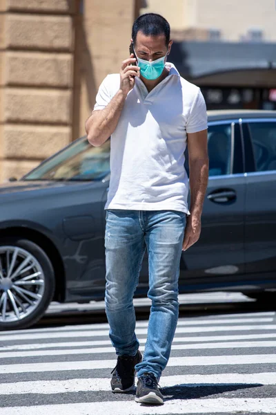 位于市中心的一个人行横道上 身穿白色马球衫 头戴防护面罩 穿着便衣的男子穿过人行横道 — 图库照片