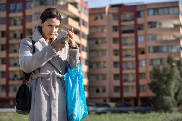Pardösülü Alışveriş Çantalı Esmer Kız Akıllı Telefonunu Şehrin Arka Planındaki — Stok fotoğraf