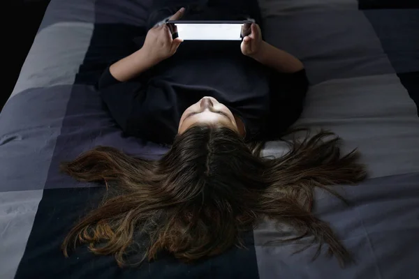 女孩躺在地上 一头乌黑的头发和一件黑色的毛衣在她的平板电脑上看一部电影 — 图库照片