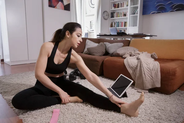 穿着黑色运动服的女孩穿着运动器材和平板电脑在家里的地毯上训练 — 图库照片
