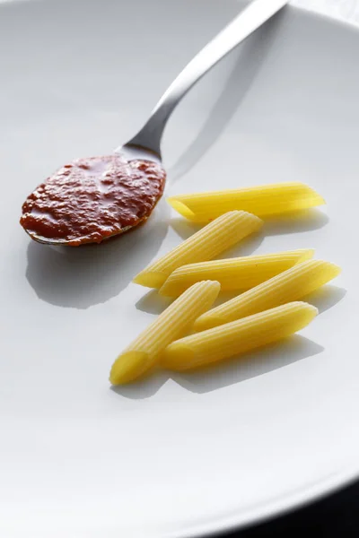 Makaron Niegotowanego Penne Łyżką Puree Pomidorowego Białym Talerzu — Zdjęcie stockowe