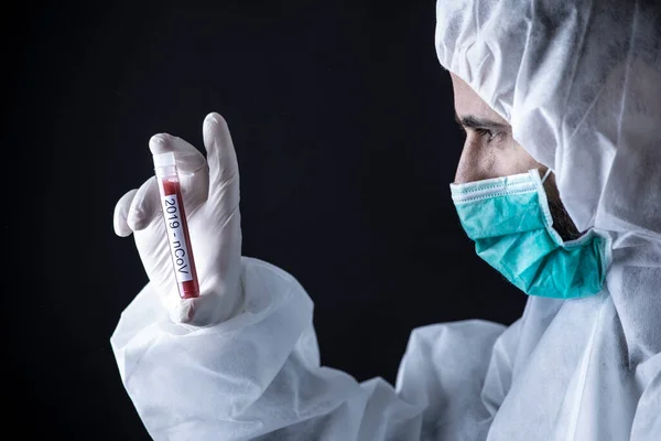 身着防护服戴口罩的医生拿着用于验血的管子 黑色背景 — 图库照片