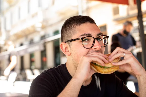 Młody Człowiek Jedzący Hamburgera Kawiarni — Zdjęcie stockowe