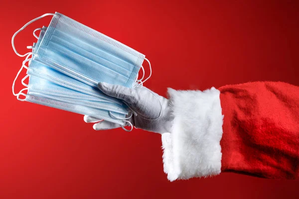 Weihnachtsmann Hand Hält Einige Chirurgische Masken Isoliert Auf Rotem Hintergrund — Stockfoto