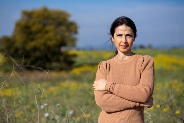 Turuncu kazaklı esmer kız hapşırırken ve dirseğiyle kendini korurken, doğa arka planında soyutlanmış.