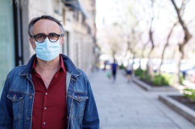 Kentsel alanda koyu renk gömlekli, maskeli ve siyah gözlüklü bir adam var.