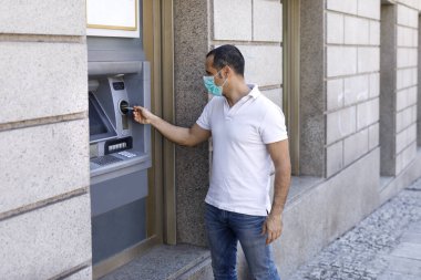 Yüz maskeli sıradan bir adam sokaktaki ATM 'den para çekiyor.