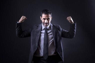 Takım elbiseli yönetici, siyah arka planda izole edilmiş kollarıyla kasların işaretini yapar.