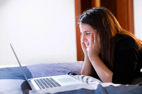 穿着黑头发和黑色衬衫的小女孩通过笔记本电脑在床上看电影 — 图库照片