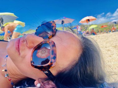 Kadın plajda güneş gözlükleriyle yatıyor.