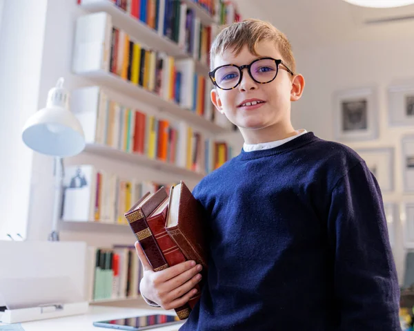 身穿眼镜套装的金发孩子站在书房里 手里拿着书 — 图库照片