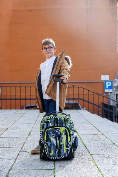 穿着眼镜和外套的金发男孩在上学路上拖着背包 — 图库照片
