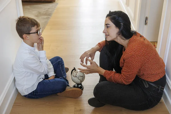 一个黑头发的成年女孩坐在家里的地板上 给一个小男孩展示了一个地球仪 — 图库照片