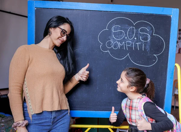 teacher and pupil are standing in front of a blackboard with the writing in Italian \