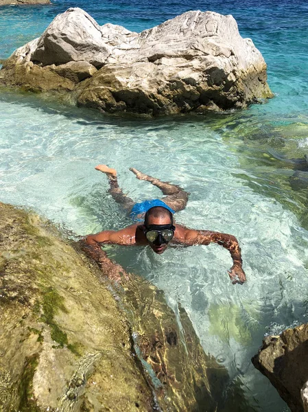 A man with a diving mask in the shallow waters of a cove in Sardinia