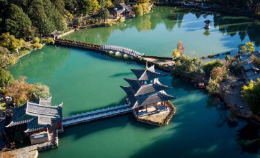 Çevresi yemyeşil ağaçlarla ve yakınlarındaki çeşitli binalarla çevrili güzel bir gölü gösteren hava manzarası.