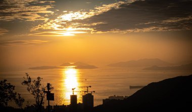 Güneş engin okyanusun üzerinde zarifçe batarken ön planda zarif bir şekilde çekilmiş bir binanın silüetiyle çarpıcı bir zemin oluşturur.