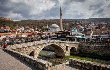 Sarmal bir nehri zarafetle kaplayan antik bir taş köprü. Arka planda görkemli bir şekilde yükselen güzel bir cami, çarpıcı bir manzara yaratıyor.