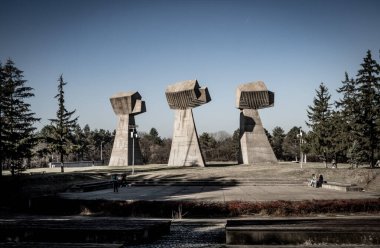 In a scenic park, there are three remarkable concrete sculptures, standing prominently amidst a lush backdrop of trees that enhance their beauty