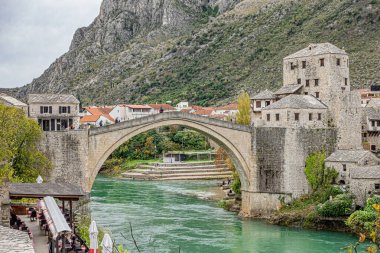 Nehir boyunca uzanan güzel bir köprü ve arka planda, yamaçta gururla duran görkemli bir kale var.