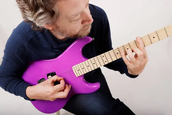 Beyaz arka planda oturan isimsiz bir adam gitar çalışıyor.