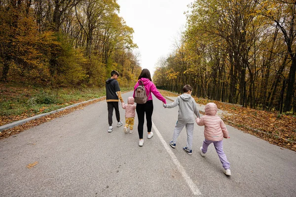 Back of mother with four kids running on road at autumn fall forest.