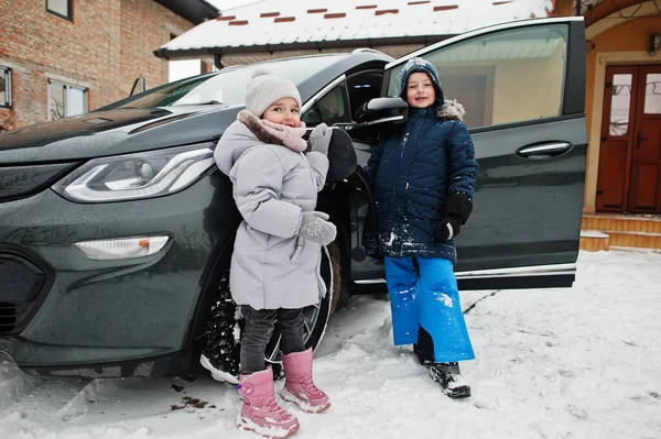 Kids charging electric car in the yard of house at winter.