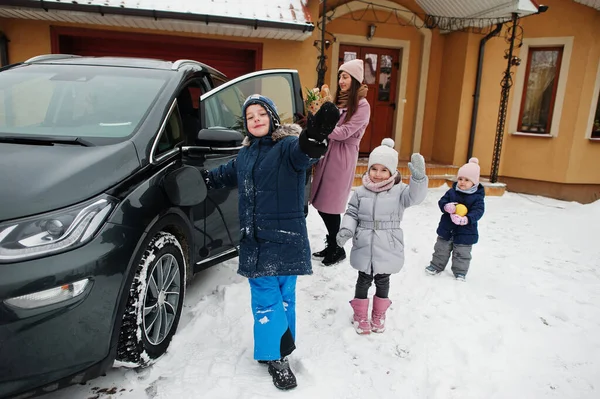 Young woman with kids hold eco bags and charging electric car in the yard of her house .