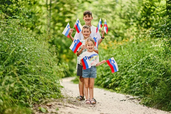 Three kids hold slovenian flags in Triglav National Park, Slovenia.