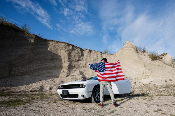 Back of man with USA flag near his white american muscle car in career.