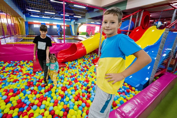 Happy kids playing at indoor play center playground. Children near colored slide with balls in ball pool.