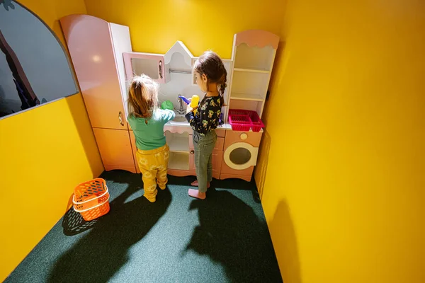 Two sisters playing at indoor kids kitchen playground.