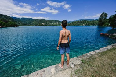 Slovenya 'nın güzel Bled Gölü manzaralı iskelede duran oğlanın arkası.
