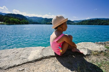 Bebeğin arkasında mayo ve şapka var. Güzel Bled Lake, Slovenya manzaralı bir iskelede oturuyor..