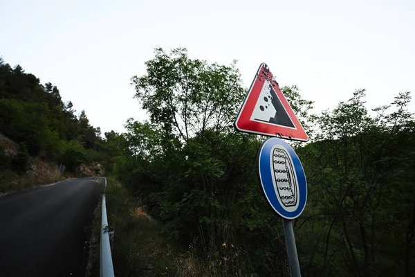 Road sign falling stones, traffic sign caution possible falling rocks with compulsory snow chains aboard car in winter.
